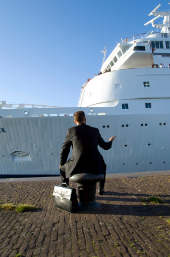 businessman sitting on mooring buoy at canal lock putting his thumb up at a cruise ship like he is hitchhiking