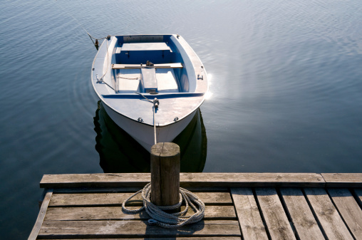 Small boat in the Swedish archipelago. Sun reflecting in the calm water. Wooden bridge with moor and rope.