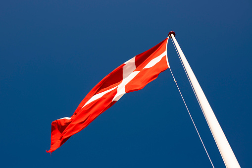 A red and white Danish flag flies against a blue sky