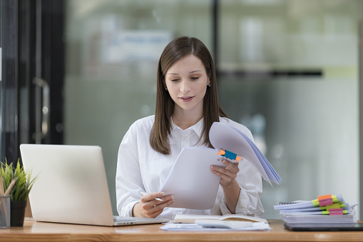 A businesswoman and accountant read reports for information, financial data, or analysis. Documents, auditor, and happy female professional check contracts, review, and bookkeeping in the office.