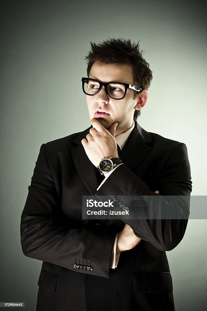 Young pensive businessman Portrait of a pensive young businessman standing with his hand on his chin and wearing thick rimmed glasses. Adult Stock Photo