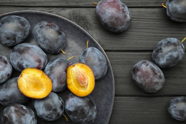 istock Fresh plums on dark plate on black wooden background 1729557474