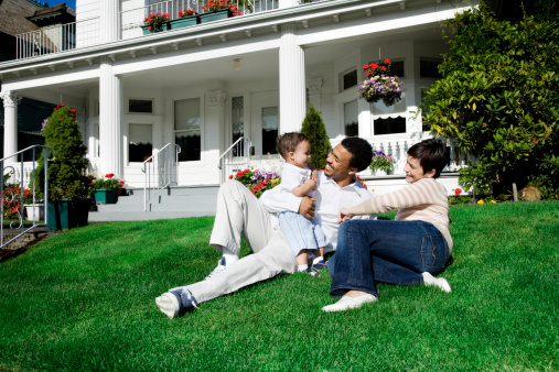 Photo of a happy family of three enjoying a sunny summer day on the lawn in front of their home.