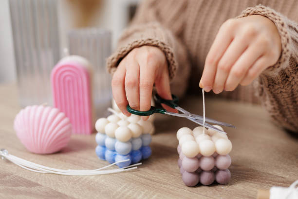 femme fabriquant des bougies à la maison, gros plan de mains féminines coupant mèche de boule boule sur table - fabrication bougie artisanale photos et images de collection