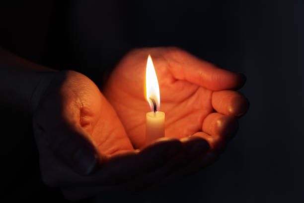 istock Two hands holding a burning candle in dark 1729566382