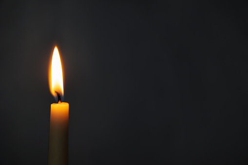 close up of burning yellow candle over dark background with copy space