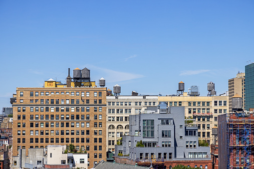 The Bowery, Manhattan, New York, USA - August 23th 2023: Old and new New York skyline with the traditional water tanks on the roofs seen from a high building on a clear summer day with blue sky