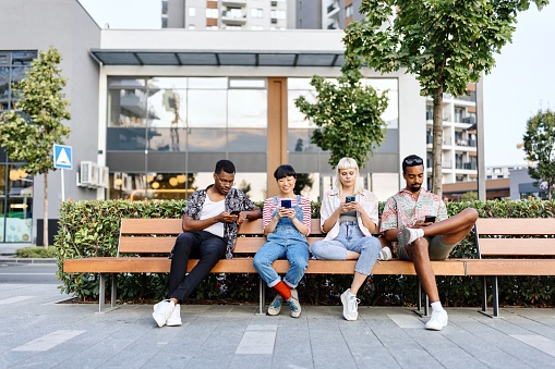 Group of multiracial people sitting on a bench and looking at their smartphones