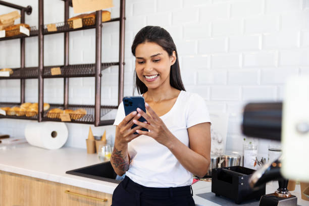 Happy female bakery owner using mobile phone standing behind the counter