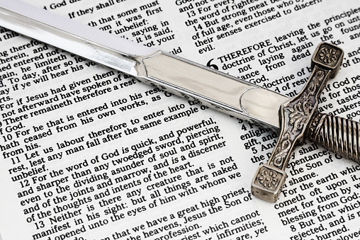 A sword on top of a (King James Version) Bible open to the book of Hebrews.  Verse 12 states:  For the word of God is quick, and powerful, and sharper than any twoedged sword, piercing even to the dividing asunder of soul and spirit, and of the joints and marrow, and is a discerner of the thoughts and intents of the heart.