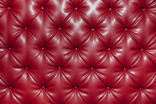 Close up background texture of red genuine leather, classic retro Chesterfield style, furniture upholstery with deep diamond pattern and buttons