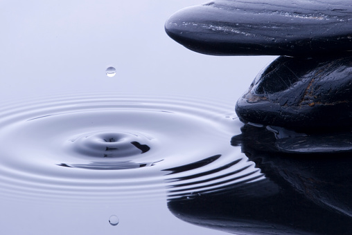 Water drop suspended in air in front of black stones.