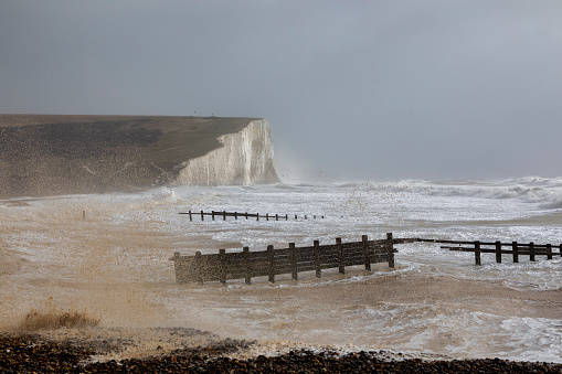 Waves roll in on Freshwater Bay in the Isle of Wight on a cloudy and windy day. Across the bay the chalk cliffs have eroded away leaving interesting rock formations.