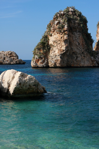 Typical Italian seascape with faraglioni (huge rocks coming out of sea) covered with mediterranean vegetation.