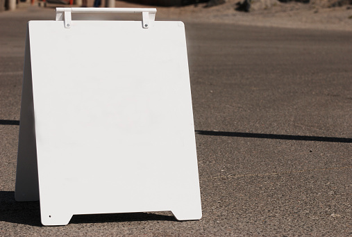 A white sign board waits for your message.  Folding board on pavement background, good copy space on the board or background right.
