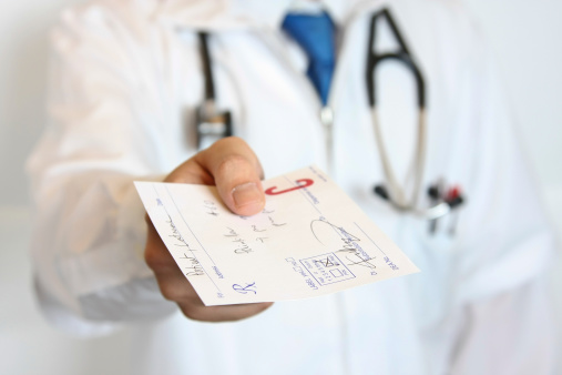 Male doctor handing a prescription to the patient.  Shallow depth of field, focused on the prescription.