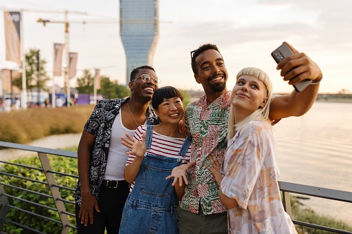 Lovely multiracial friends taking selfies next to the river
