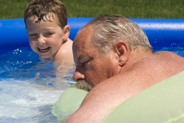 Sneaking up on Pee Pa Boy sneaks up on his grandfather who is pretending to sleep on a raft in the child's swimming pool. sleeping grandpa stock pictures, royalty-free photos & images