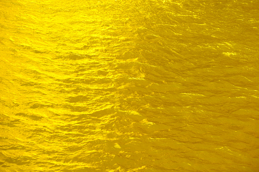 Defocus blurred transparent gold colored clear calm water surface texture with splashes reflection. Trendy abstract nature background. Water waves in sunlight with copy space. Yellow  watercolor shine.