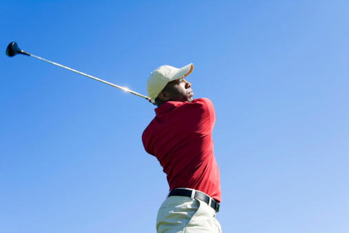 Photo of a golfer swinging his club against a clear blue sky.