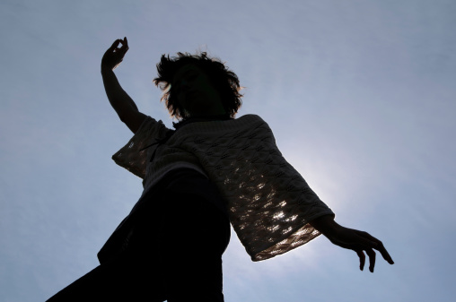 Young Woman Dancing Silhouetted by Sun, Blue Sky Clouds Background