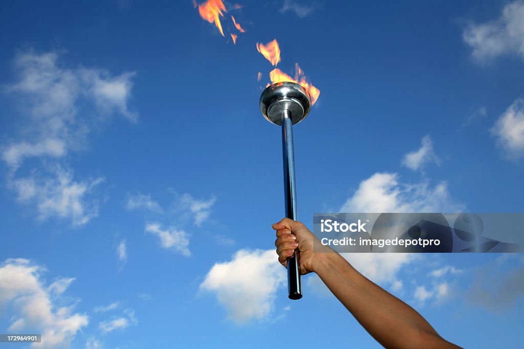 glory of holding flaming torch silhouetted hand holding burning flaming torch over cloudy sky.  International Multi-Sport Event Stock Photo