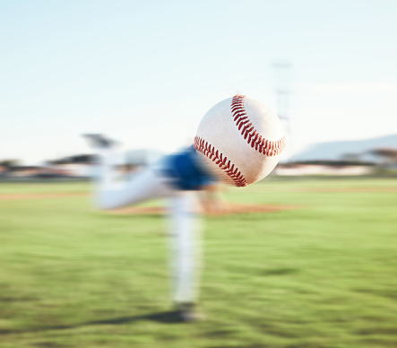 Low angle selective focus view of a baseball in grass with outfield fence in the background