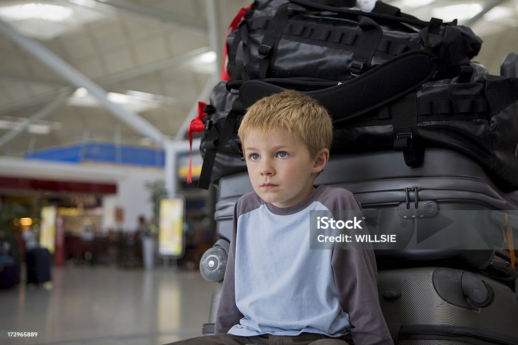 waiting at the airport A young boy is sitting on the luggage trolley with the luggage for his family behind him and is staring upward. His flight has been delayed. The airport shops are seen in the background.canon eos 5D camera 4-5 Years Stock Photo