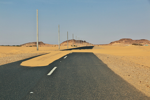 Empty Open Desert Road inside the arid vast Desert Landscape of the Sossusvlei Nambib Desert of Namibia. Giant Sand Dunes roadside the Highway. Panorama Shot under blue summer skyscape. Namibian Desert, Sossusvlei, Namibia, Southern Africa.