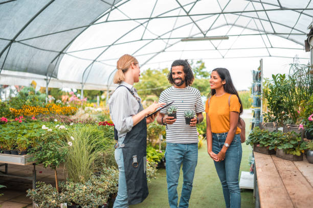 istock Diverse Pair Acquires Small Potted Plants with Support from Caucasian Gardener 1729700823
