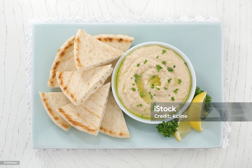 Rectangular plate of pita slices with hummus, and lemon Healthy snack of hummus, with olive oil and parsley served with pita bread.  Hummus - Food Stock Photo