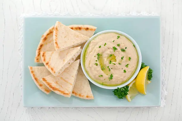 Healthy snack of hummus, with olive oil and parsley served with pita bread. 