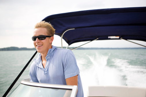 young man driving a boat with an excited smile.