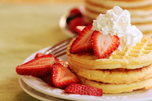 Waffles with strawberries and whipped cream.  Stack of pancakes in the background with raspberries and blueberries.  