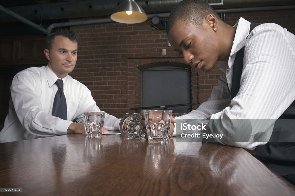 Drinking Too Much Focus on young man with a drinking problem. He bends his head in despair and shame. Out of focus bartender in background looks at him with concern.Check out my Addiction Stock Photo