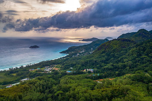 Aerial view of Grand Anse Beach at the Mahe Island, Seychelles, with heavy clouds, Indian Ocean, local villages, mountains and rain forests.