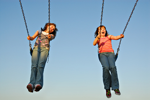 Twin sisters swinging in sync at a park.