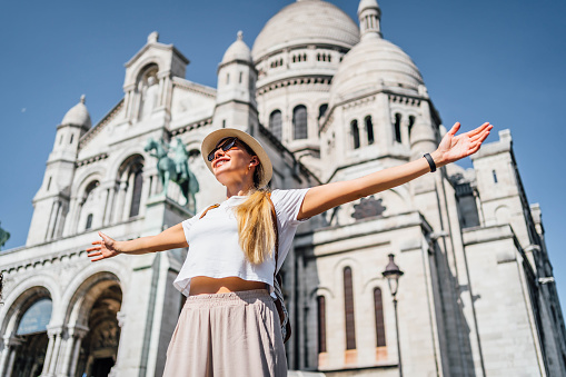 Young happy woman in front of the Sacré Coeur Basilica de Montmartre in Paris, France