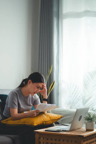 asian woman sitting on sofa worried having bill payment problems with bank papers mortgage debt and cost of living. - credit crunch wallet home finances credit card imagens e fotografias de stock