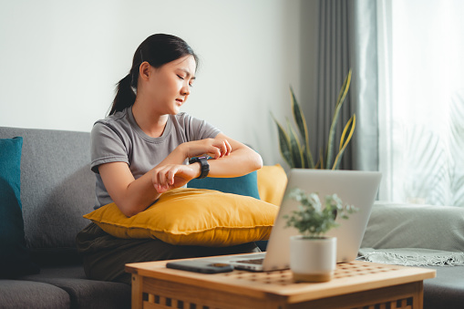 Asian woman suffering from irritate dry skin and scratching her skin sitting on sofa in living room at home.