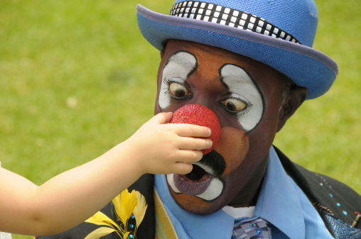 Clown looking cross eyed at  his nose while  a child squeezes it.