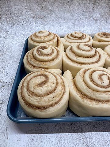 Stock photo showing close-up, elevated view of a baking tray containing rows of uncooked, ready to bake homemade, cinnamon swirl danish pastries.