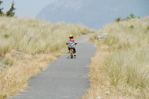 Young boy rides his bike on a path through sand dunes.