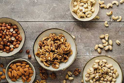 Organic nuts based food snacks mix on wooden table. Top view of assortment of dry fruit bowls on wooden surface.