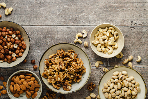 Healthy nuts based food snacks mix on wooden background. Top view of assortment of dry fruits in bowls on wooden surface.