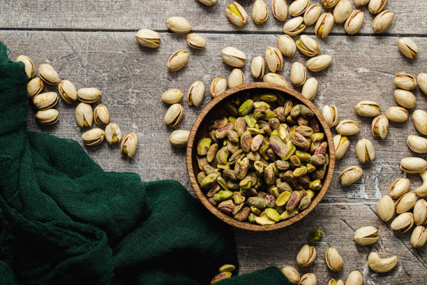 istock Salted pistachios in a bowl with shells on wooden surface 1729805266