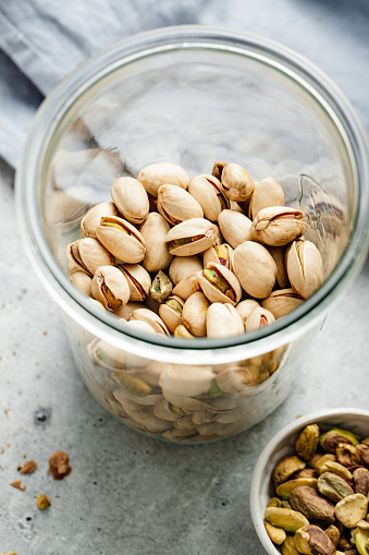 Top view of a glass jar with pistachios on the kitchen table. Pistachios with shells in a glass container and bowl on kitchen coutner.