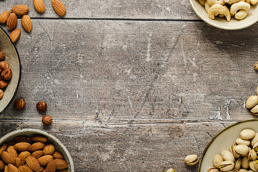 Top view of assortment of dry fruits in bowls on wooden surface with copy space. Healthy dry fruit nut bowls arranged as frame border on wooden background.