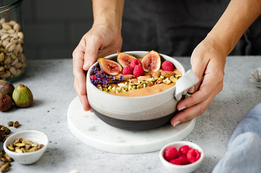 Close-up of a woman serving healthy breakfast. Female hands with smoothie bowl garnished with dry fruits and berries.