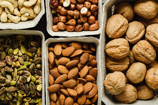 Assortment of dry fruits in paper containers. Full frame top view of Cashew, roasted hazelnuts, whole walnuts, almonds and peeled pistachio in paper bowls.
